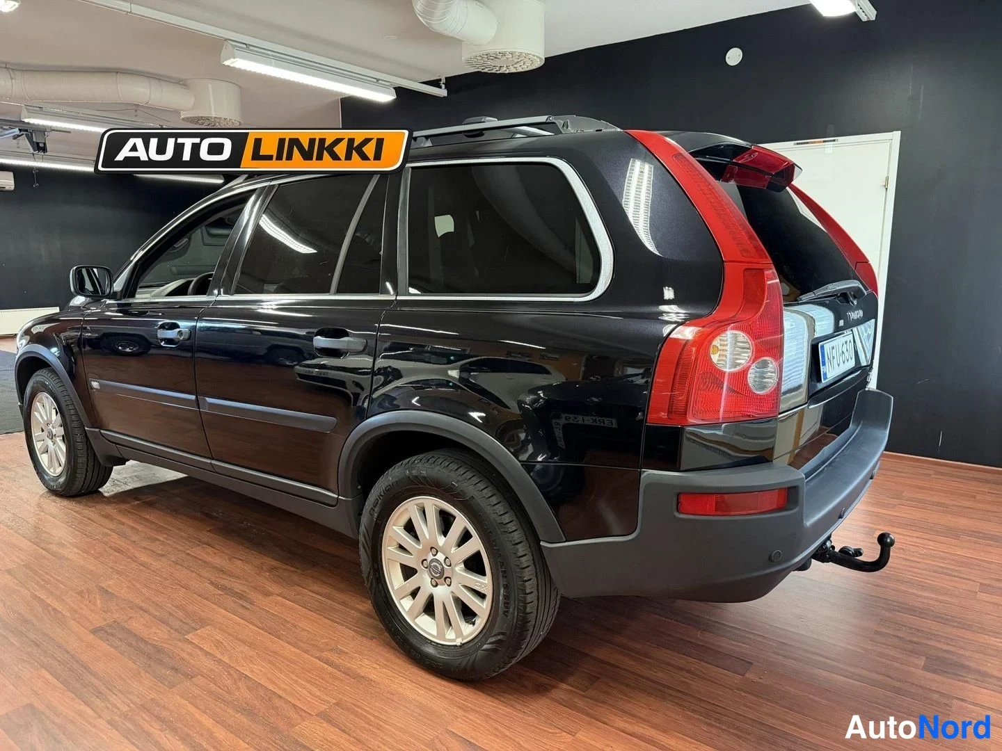 Takaviisto: Mustan Volvo XC90:n takakulma sisätiloissa, punaiset takavalot, vetokoulu ja rekisterikilpi näkyvissä.