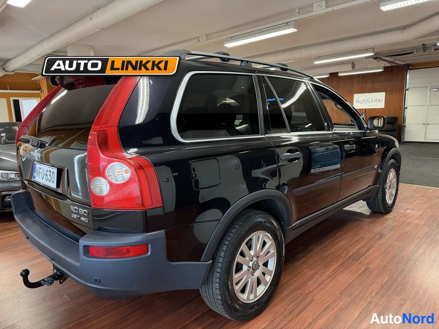 Takaviisto: Mustan Volvo XC90:n takakulma sisätiloissa, takavalo, XC90-tunnus, vetokoulu ja rekisterikilpi näkyvissä.
