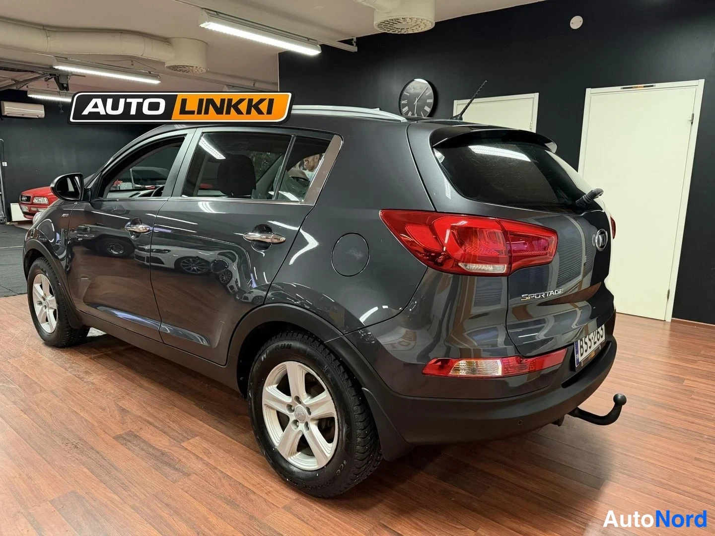 Takaviisto: Auton takanäkökulma vinosti oikealta, tummanharmaa Kia Sportage takapuoli ja kylki sisätiloissa.