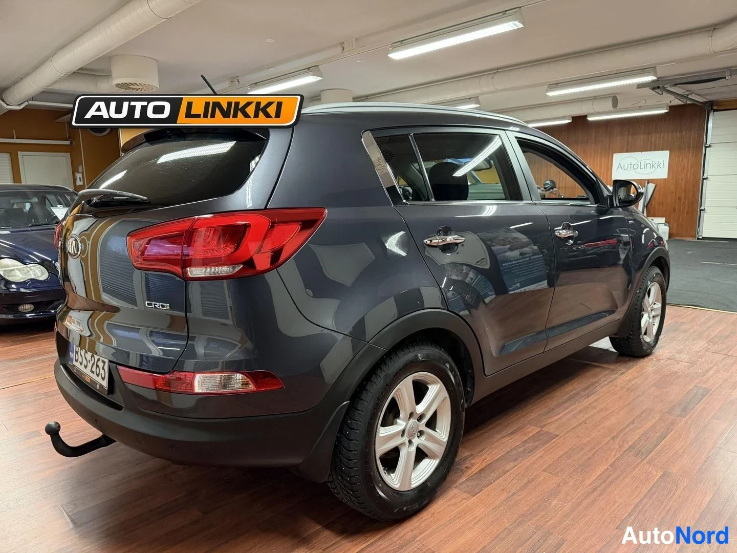 Takaviisto: Auton takanäkökulma vinosti vasemmalta, tummanharmaa Kia Sportage takapuoli ja kylki sisätiloissa.