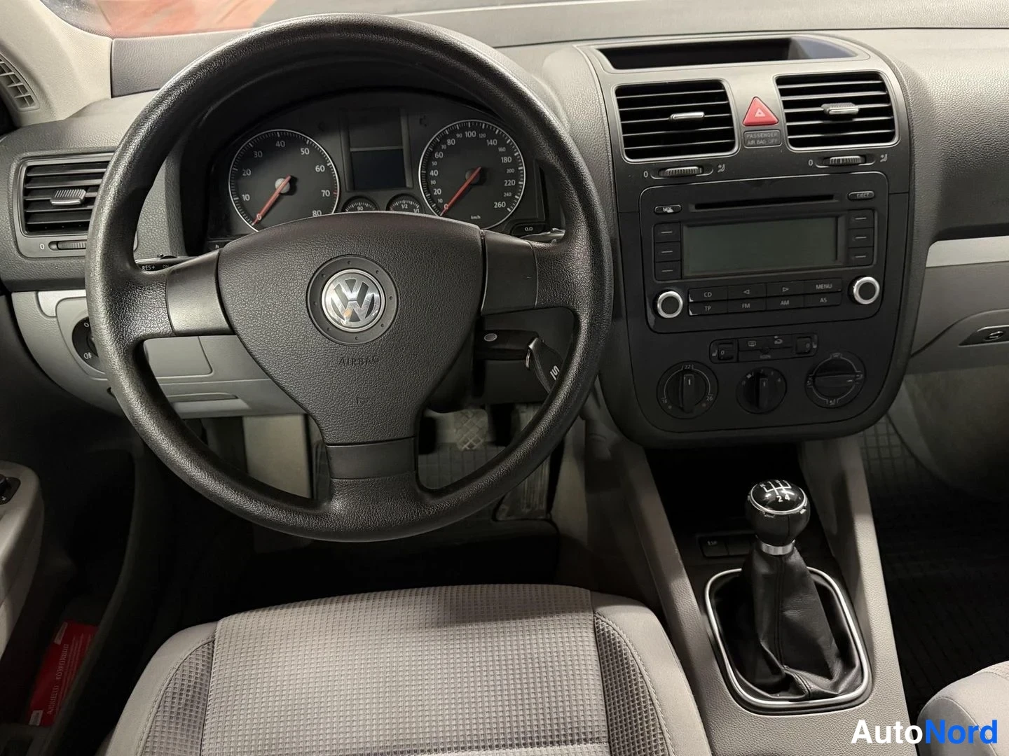 Muu: Ohjaamo VW-merkillä varustetulla ratin ja manuaalivaihteistokahvalla, kojelauta ja radiopaneeli näkyvissä.