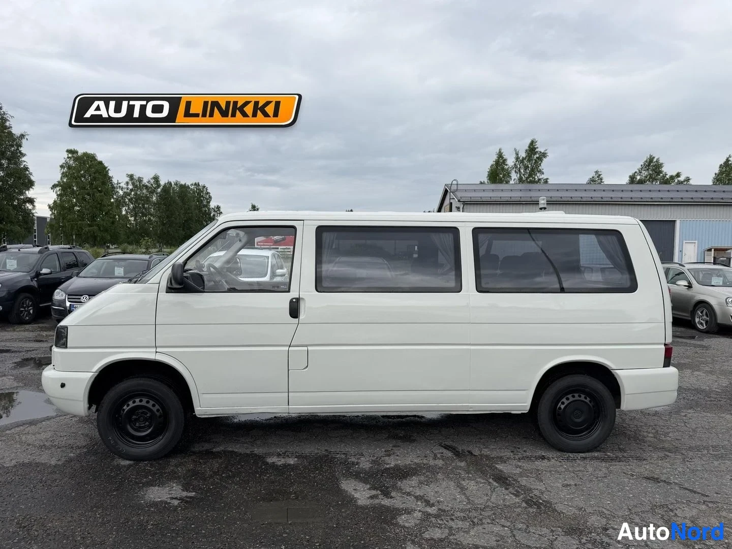 Sivulta: Valkoisen Volkswagen Caravellen sivuprofiili, vasen kylki kuvattu auton nokan osoittaessa vasemmalle.