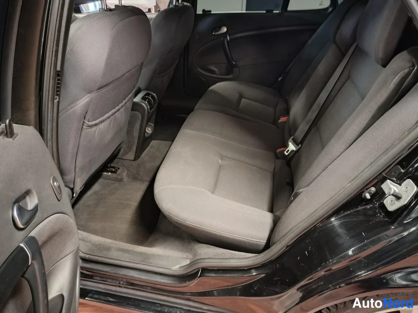 Takaa: Saab 9-5:n takapenkki toisesta takaovesta katsottuna: tummanharmaa kankainen penkki, etuselkänojen takapuolet ja musta ovipaneeli näkyvät.
