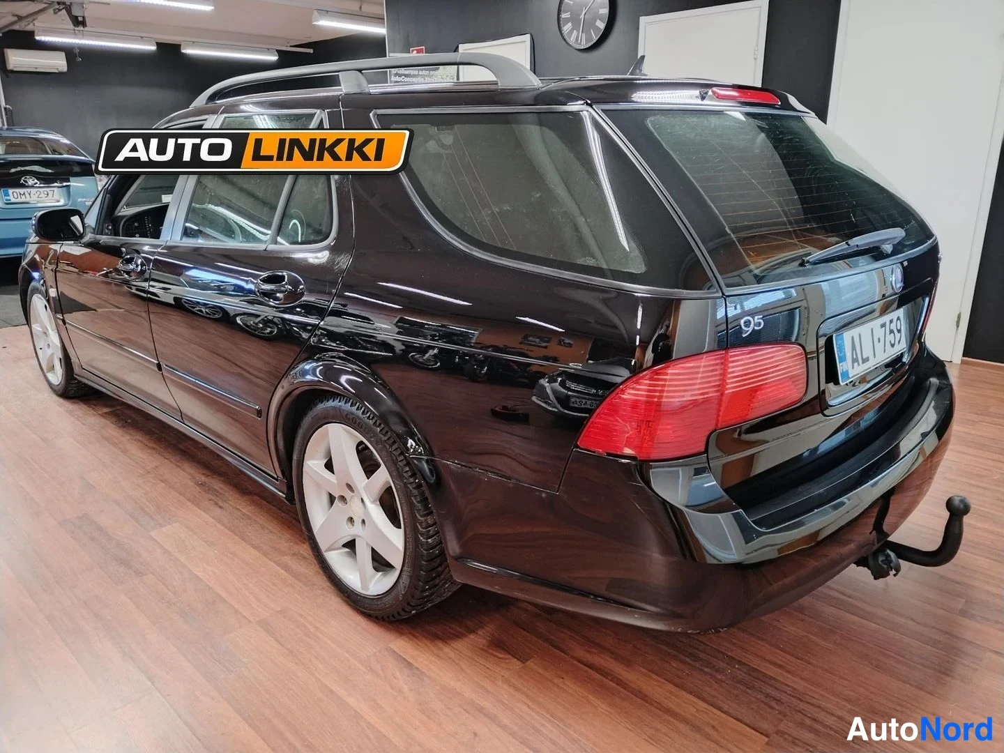 Takaviisto: Mustan Saab 9-5 -farmarin takakulmatäkki, rekisteritunnus, perävaunun koukku ja kattokaiteet näkyvät.