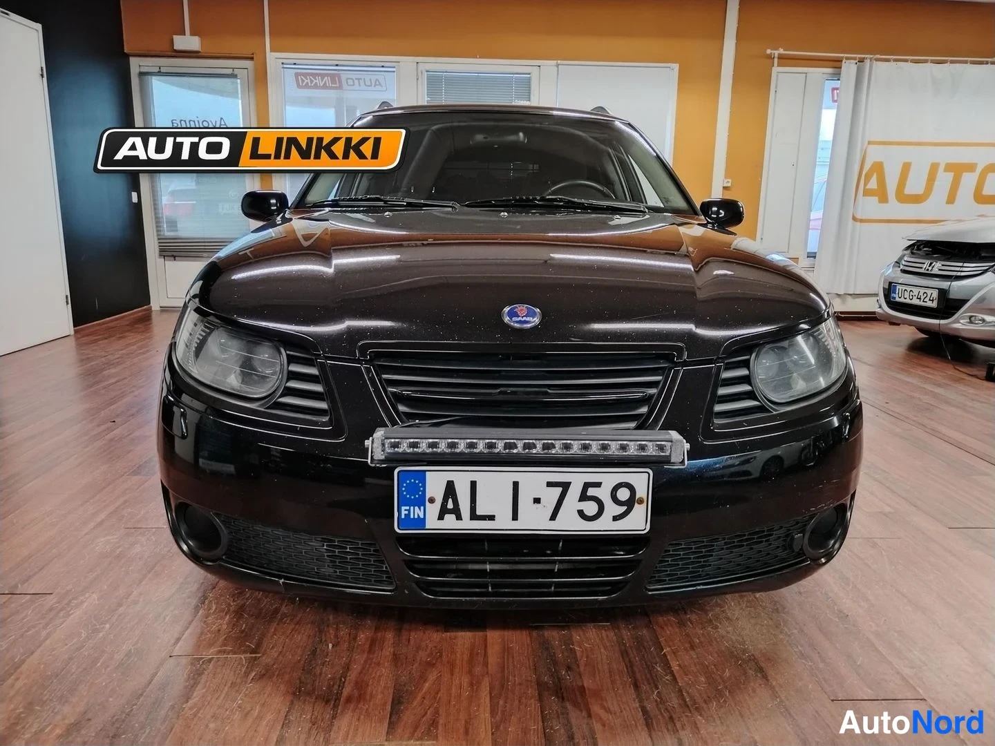 Edestä: Mustan Saab 9-5 -farmarin keula suoraan edestä, etugrilli, ajovalot ja rekisterikilpi näkyvissä.