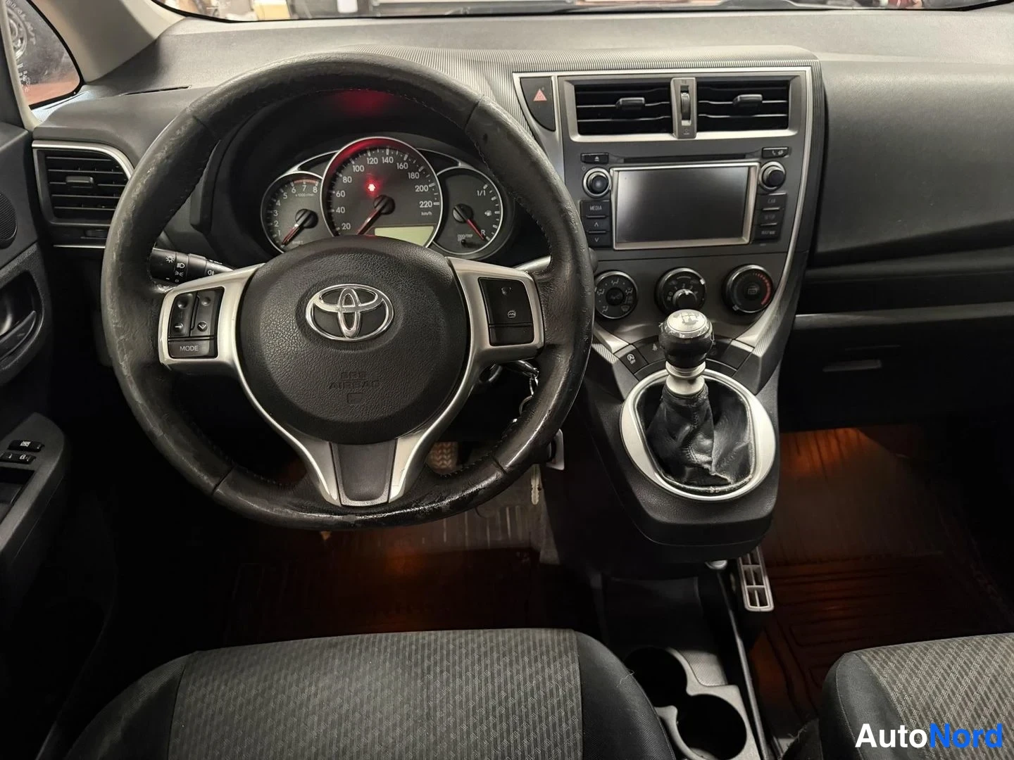 Muu: Auton sisätilat: ohjauspyörä Toyota-merkillä, mittaristo, kosketusnäyttöradio, manuaalivaihteisto ja tummat penkit.