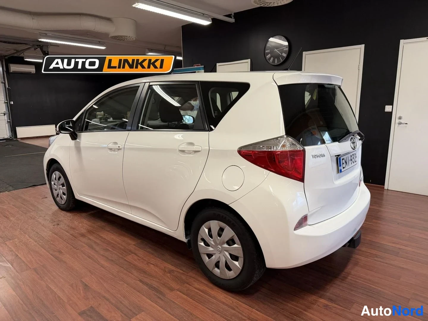 Takaviisto: Valkoinen Toyota Verso-S takaosa viistosti sisätiloissa, peräkilpi ja takavalot näkyvissä.