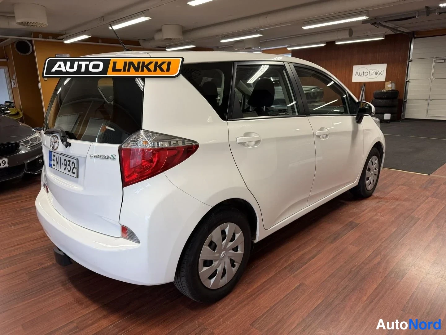 Takaviisto: Valkoinen Toyota Verso-S takaosa viistosta sisätiloissa, peräkilpi ja takaluukun logo näkyvissä.