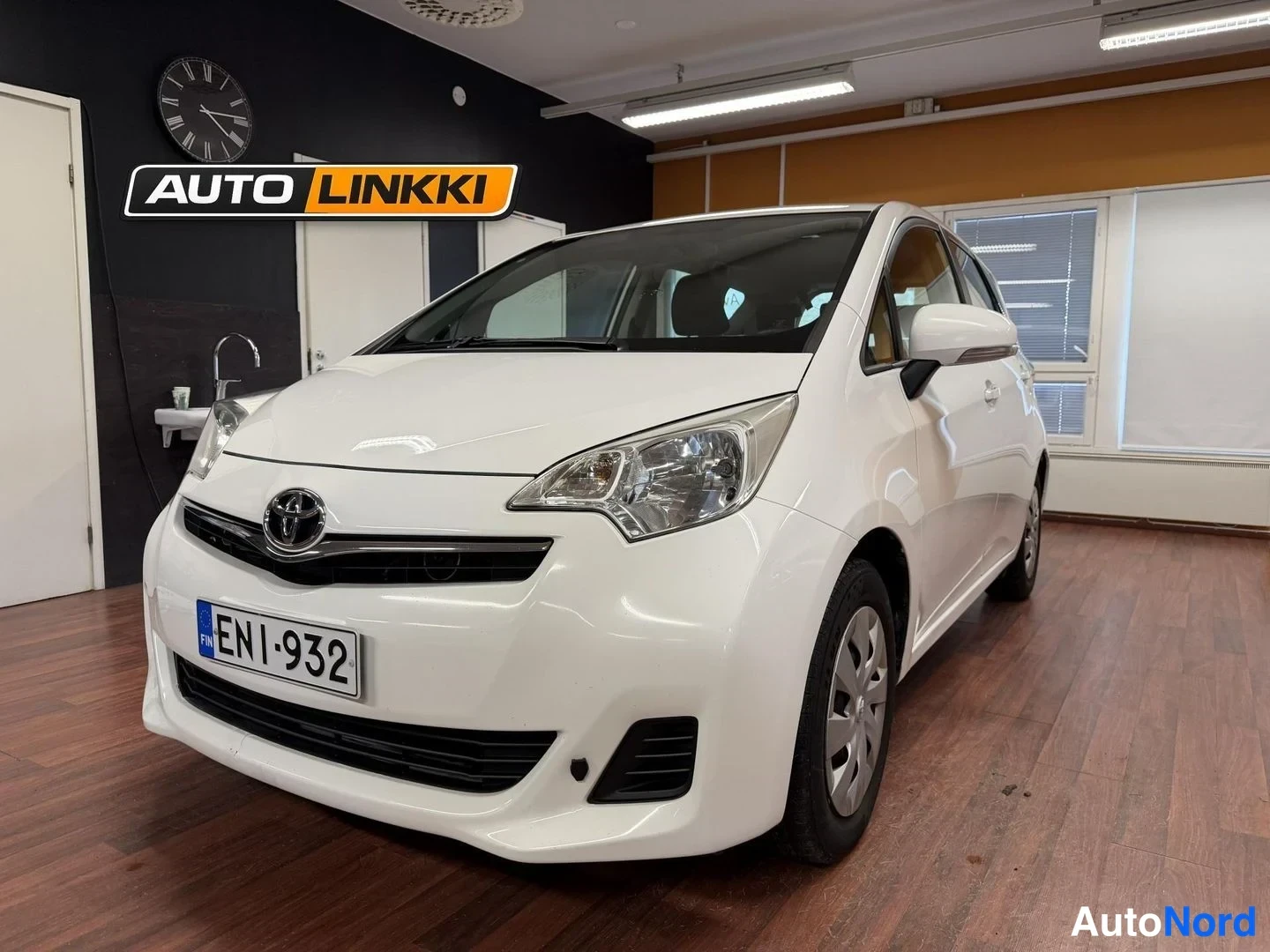 Etuviisto, nokka vasemmalle: Valkoinen Toyota Verso-S etuosa ja oikea kylki sisätiloissa, rekisteritunnus.
