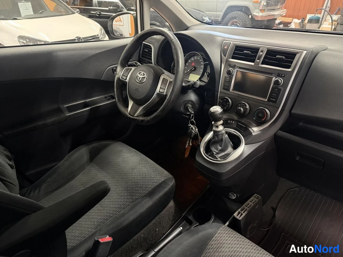 Muu: Auton ohjaamo: musta sisusta, ratissa Toyota-merkki, käsivaihtoeija ja kosketusnäyttö.