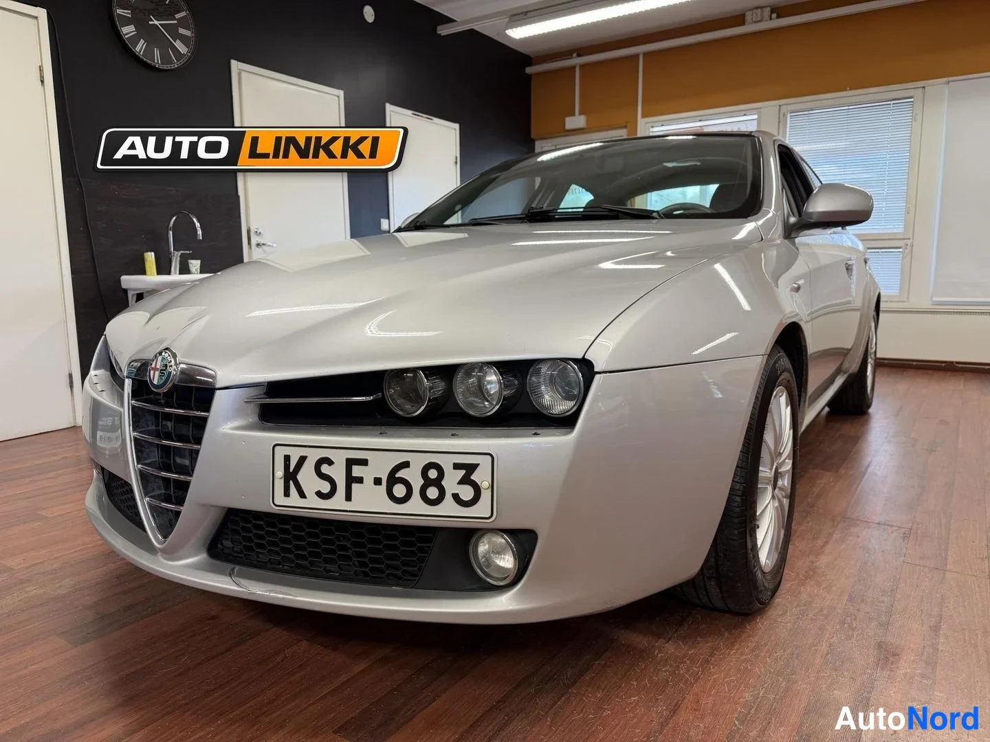 Etuviisto, nokka vasemmalle: Hopeanvärinen Alfa Romeo 159 -sedan etukolmesta-otoksessa oikealta sivulta, rekisterikilpi näkyvissä.
