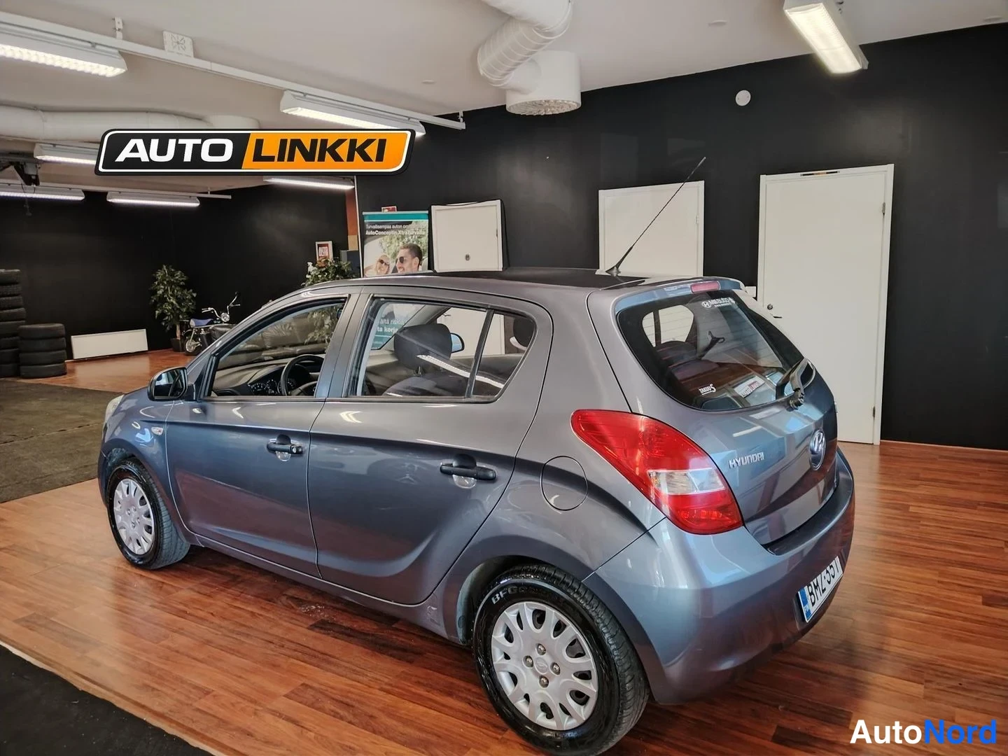 Takaviisto: Hyundai i20 -henkilöauto harmaana taka­kulmasta sisätiloissa, takavalo ja takaosa näkyvissä.