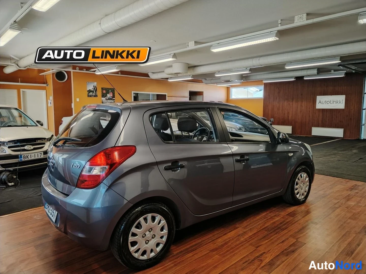 Takaviisto: Hyundai i20 -henkilöauto harmaana taka­kulmasta sisätiloissa, takavalo ja oikea kylki näkyvissä.