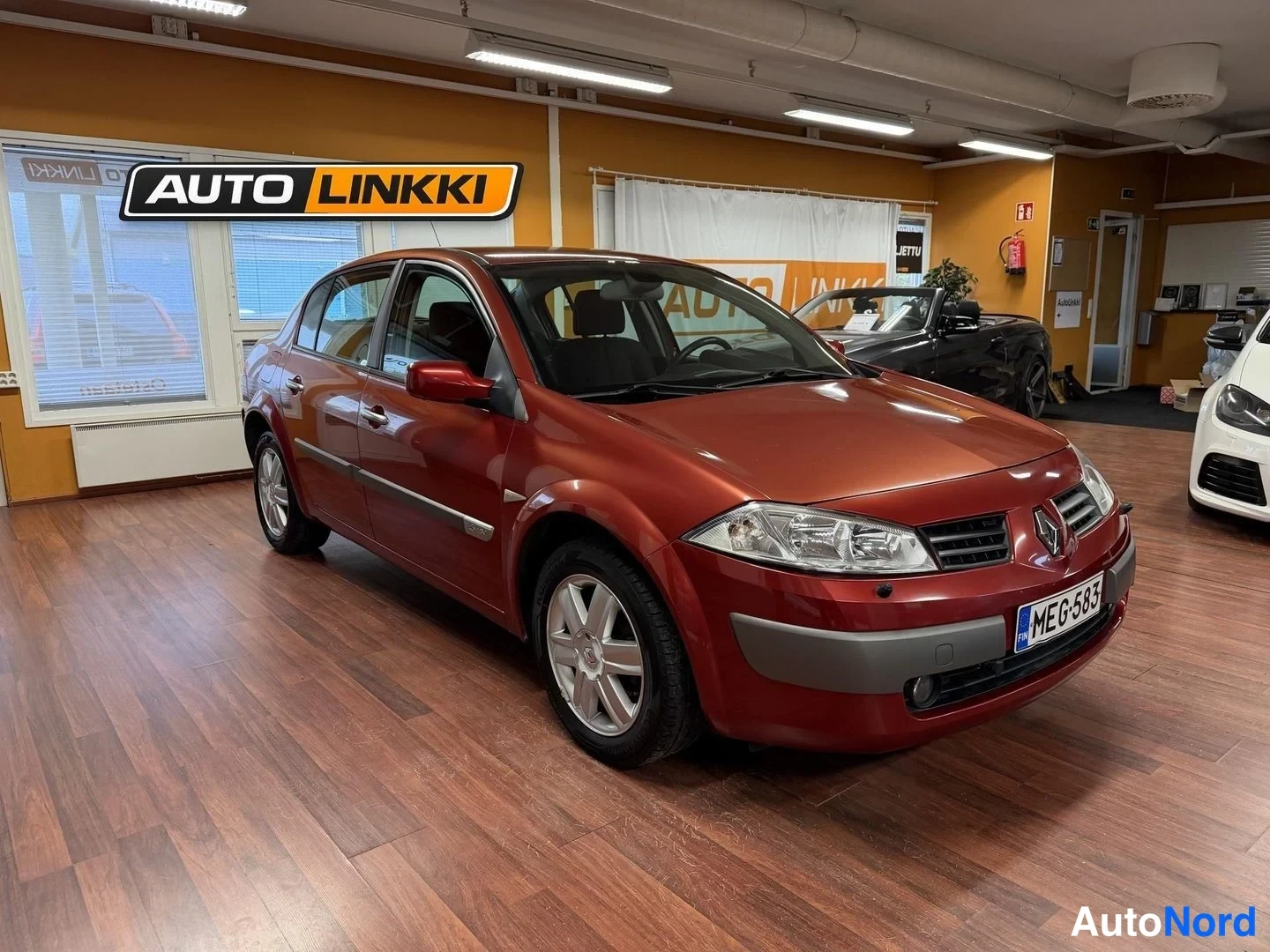 Etuviisto, nokka oikealle: Punaisen Renaultin etukulma oikealta, rekisterikilpi,Auto Linkki -logolla varustetussa autosalonissa.