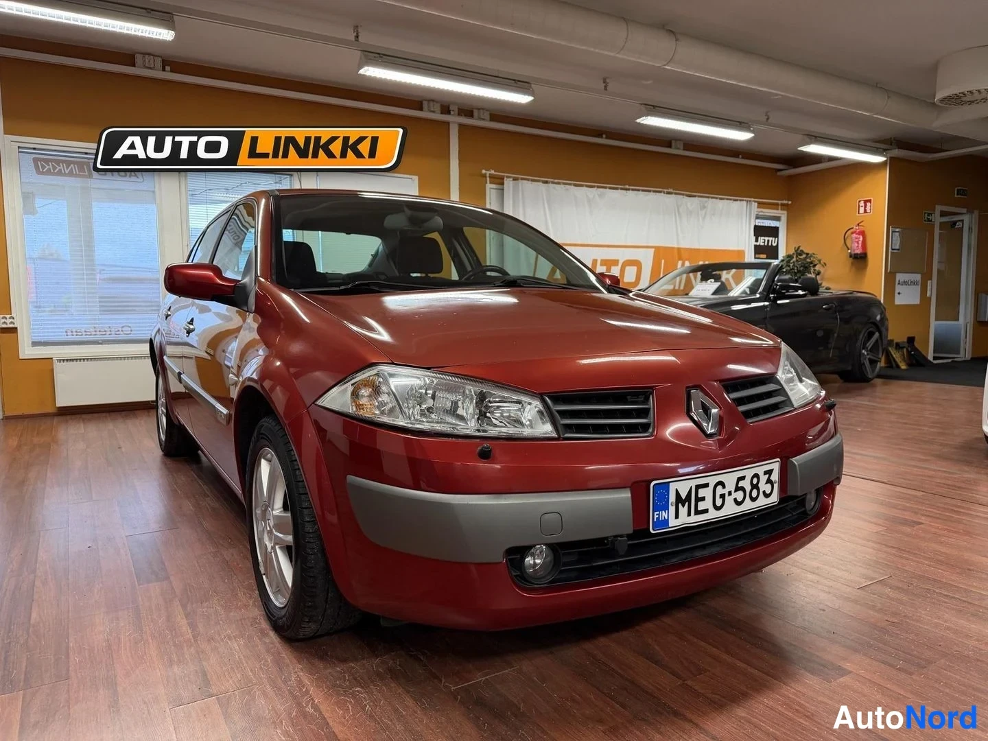 Etuviisto, nokka oikealle: Punaisen Renaultin etukulma oikealta, rekisterikilpi, autosalonin sisätiloissa.