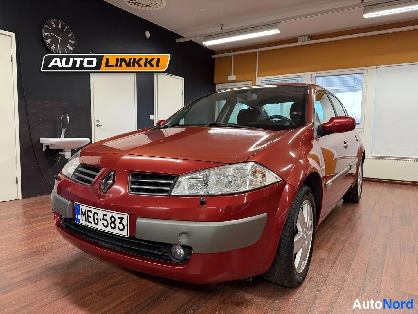 Etuviisto, nokka vasemmalle: Punaisen Renaultin etukulma vasemmalta, rekisterikilpi, autosalonin sisätiloissa.