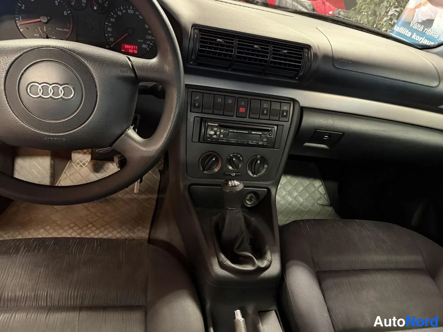 Muu: Audi A4:n kojelauta ja keskikonsoli lähikuvassa: Pioneer-radio, lämminilmapuhaltimien säätimet ja manuaalivaihteen keksi; mittaristossa lukema 302277 km ja päiv