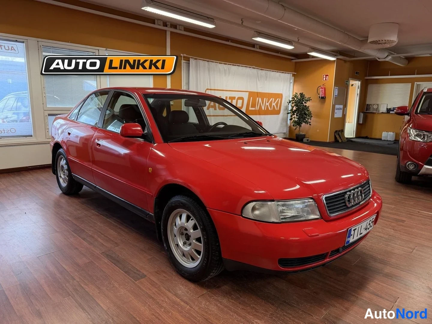 Etuviisto, nokka oikealle: Punainen sedanin kylki- ja keulaosa näkyvissäAuto Linkin showroomissa, nokka kuvan oikeassa reunassa.
