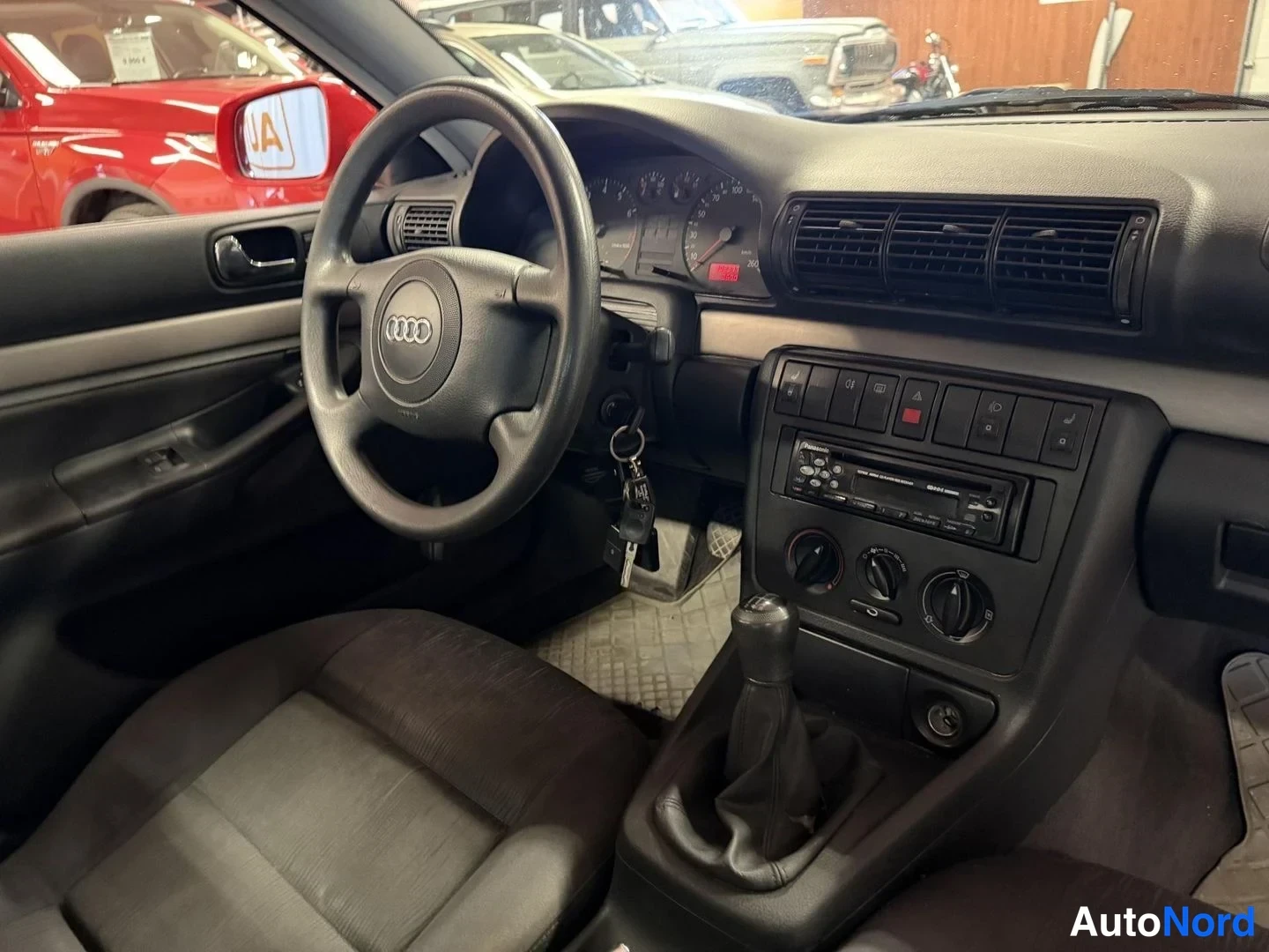 Muu: Audi A4:n sisätilat: tumma ohjaamo, Audi-merkillinen ohjauspyörä, mittaristo ja Pioneer-radiopaneeli keskikonsolissa; manuaalivaihteen keksi ja kaasulämppäistar
