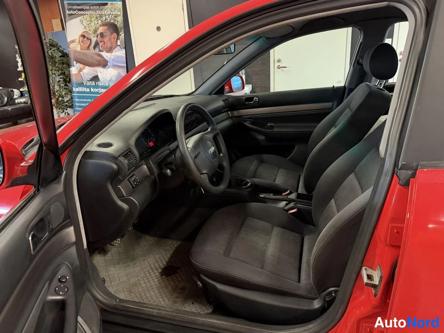 Muu: Audi A4:n etuistuintila ja ohjaamo avatusta etuovesta kuvattuna; punainen koriväri näkyy oviaukon reunassa.