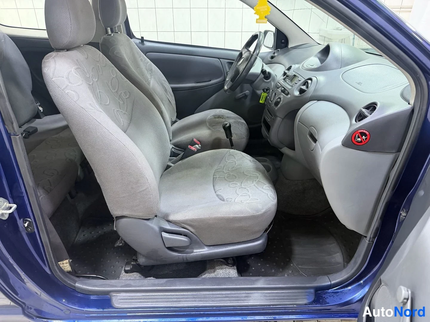 Etuviisto: Toyota Yarisin etupenkit ja kojelauta harmaana kankaana kuljettajan ovi auki.