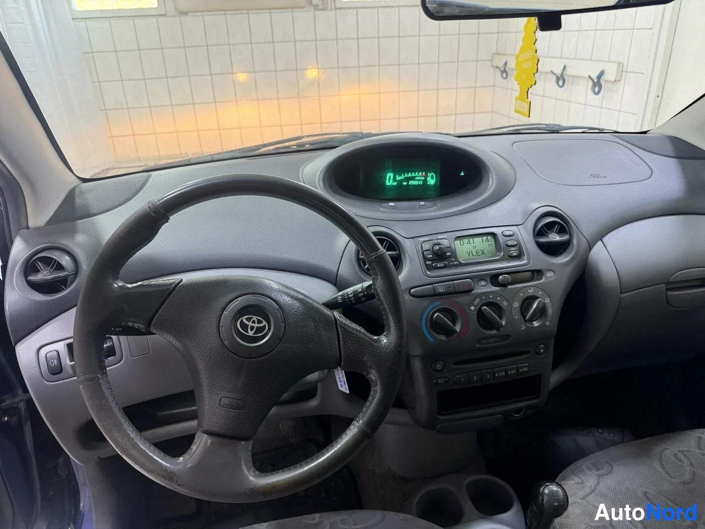 Muu: Toyota Yariksen ohjaamo: Toyota-merkkinen ratto, keskellä kojelautan digitaalinäyttö, radio ja ilmastointisäätimet.