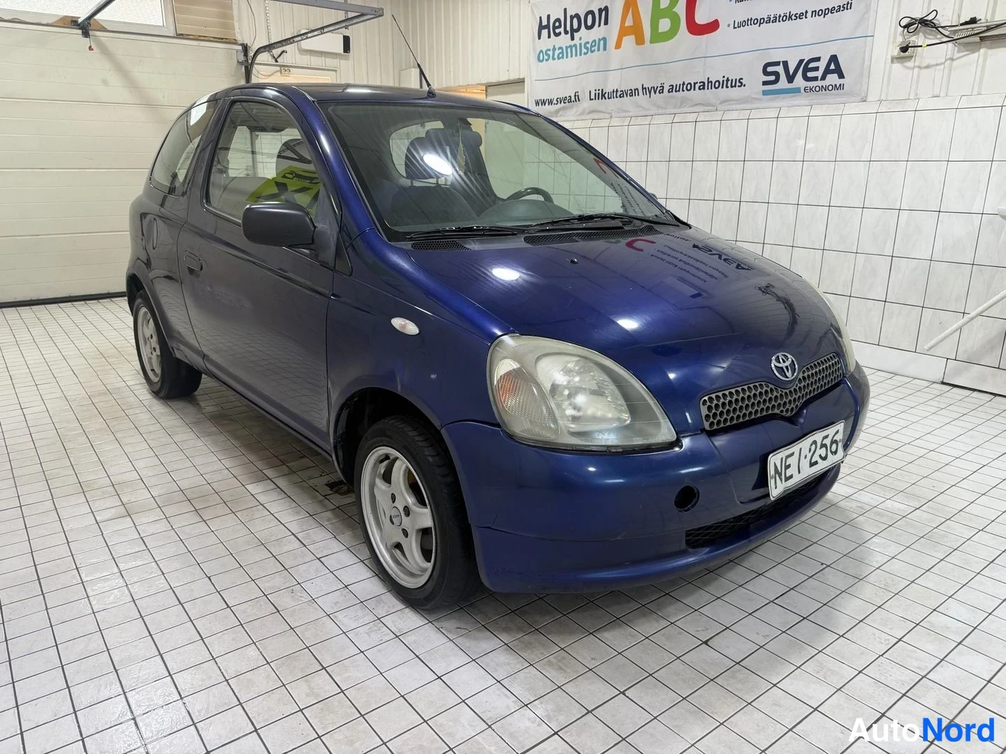 Etuviisto, nokka oikealle: Sininen Toyota etuvetoa korostuvalla keulalla etuviistosta oikealta; etusäleikkö, Toyota-merkki ja kilpi näkyvissä.