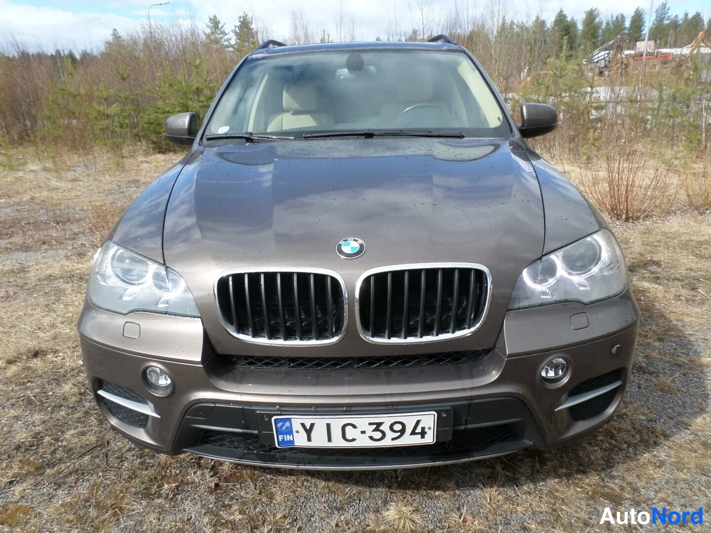 Edestä: Suora etukuvma ruskeasta BMW X5 -maastoautosta. Kuvassa näkyvät etuvalot, reikäpelti, etupuskuri ja takaluukku. Rekisterinumero on.
