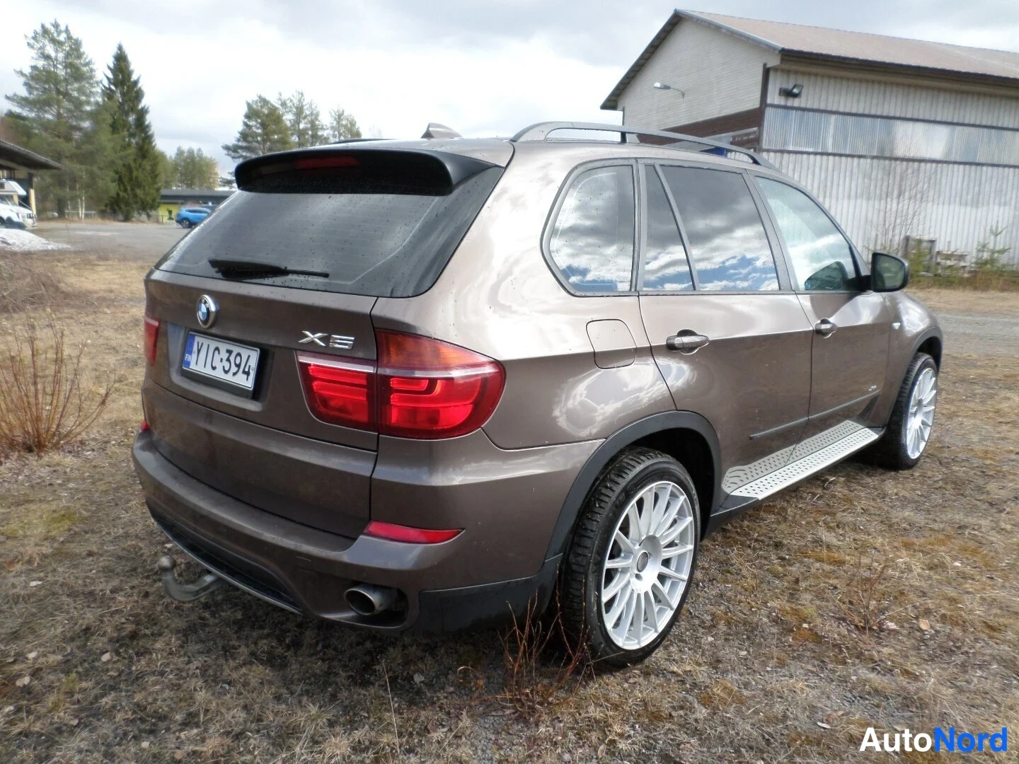 Takaviisto: Takakuplissa oleva kuva ruskeasta BMW X5 -maastoautosta. Kuvassa näkyvät takavalot, takapuskuri, sivutankki ja takarengas. Takaluukun oikealla puolella lukee 'X