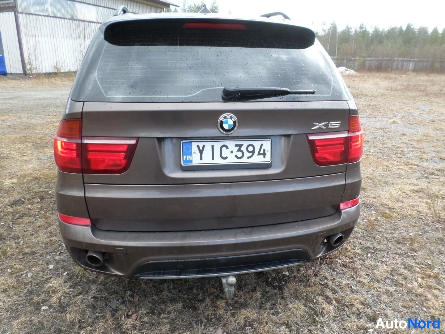 Takaa: Suora takakuva ruskeasta BMW X5 -maastoautosta. Kuvassa näkyvät takavalot, takapuskuri, takakontti ja vetoputki. Vetoputki on kiinnitetty ajoneuvon alapuolelle.