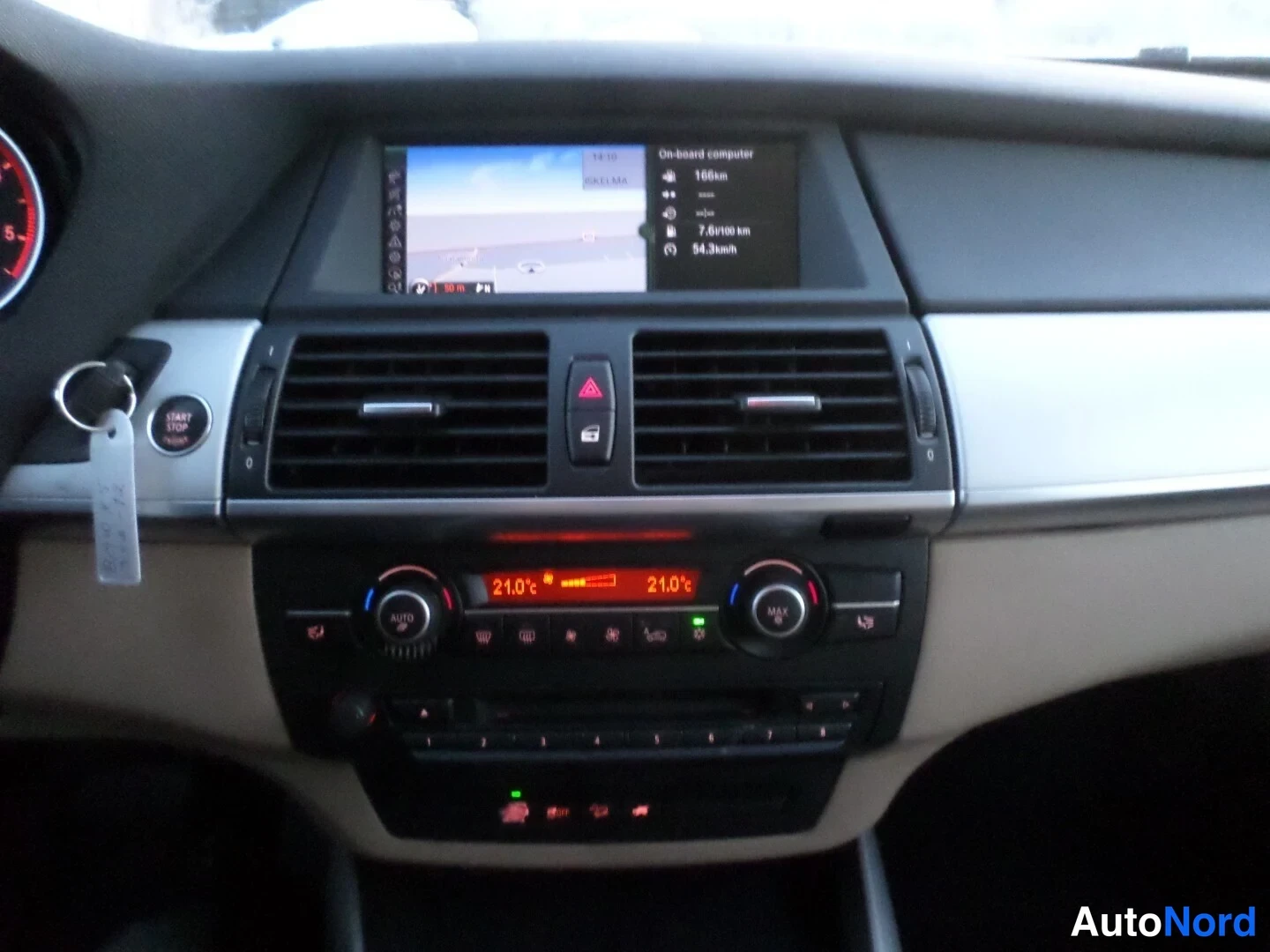 Muu: Sisäkuva: kojelaudan keskiosa, jossa näytöllä Onboard computer 168km, 7.8l/100km ja 94.3kmh, Start/Stop-nappi ja avain, kaksi säätöruutua, kaksivyöhykelämmitys