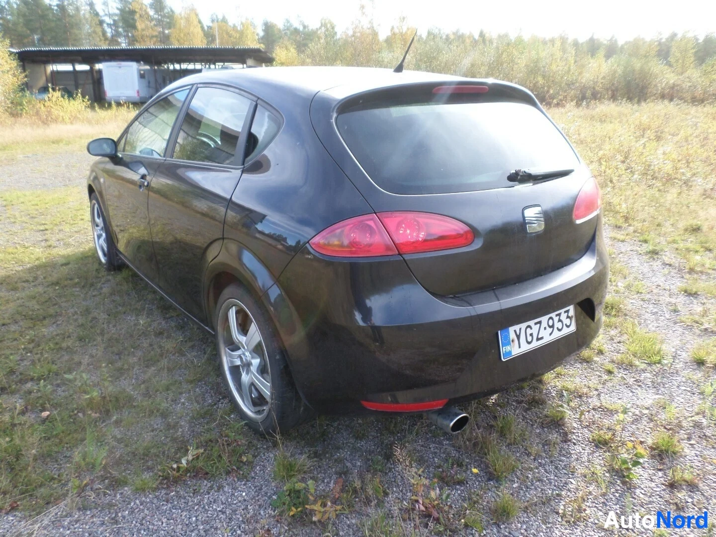 Takaviisto: Mustan henkilöauton takakulma kolmesta neljänneksestä, rekisterikilpi.