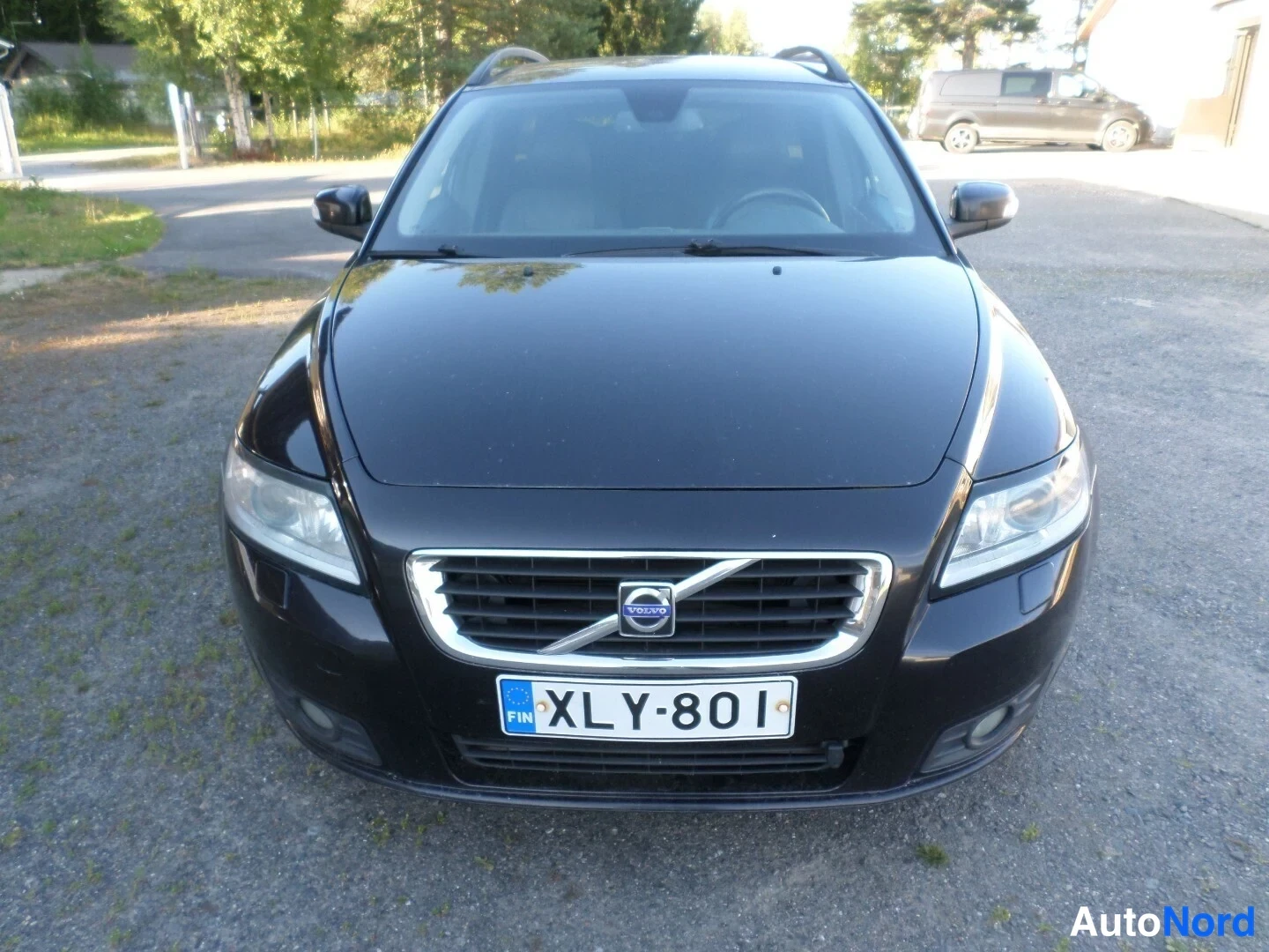 Edestä: Mustan farmariauton suora etunäkymä, rekisteritunnus, Volvo-merkki etusäleikössä.