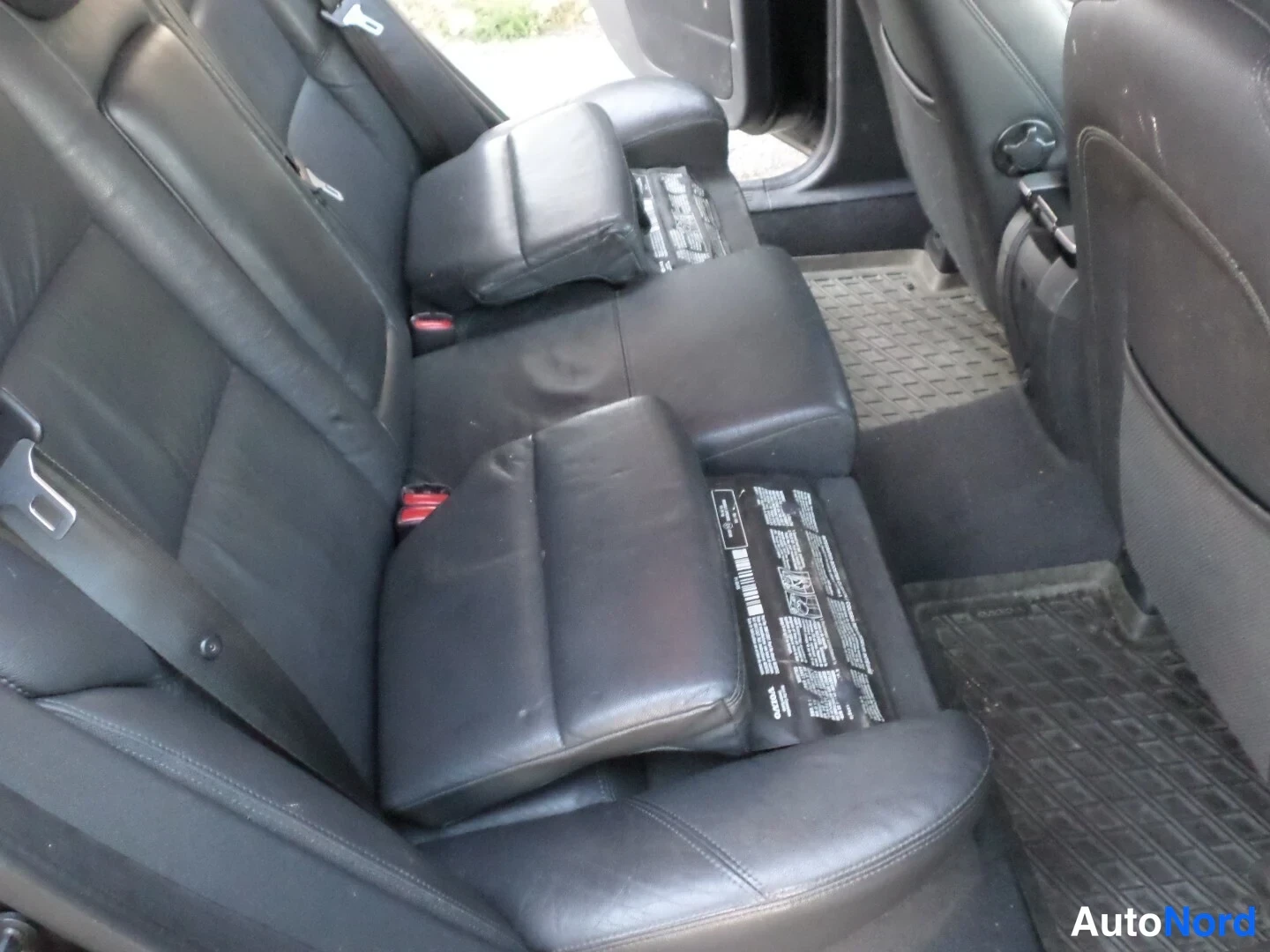 Takaistuimet: Black leather rear bench seat with a central armrest and folded-down headrests.
