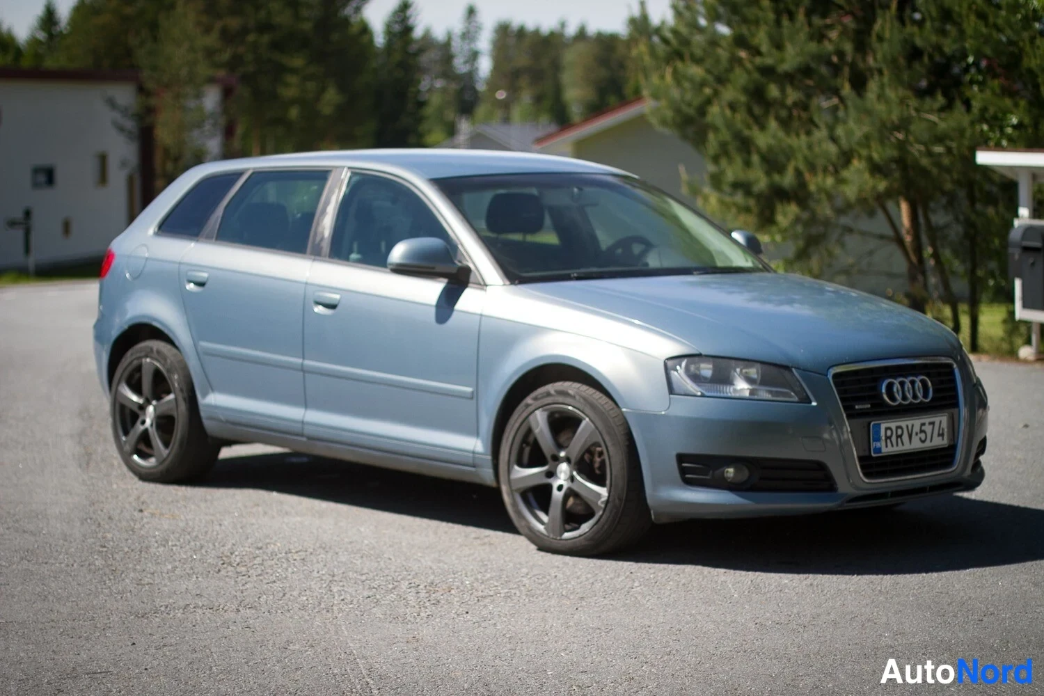 Etuviisto, nokka oikealle: A light blue Audi station wagon on asphalt. The front grille with four rings is visible along with the driver's side flank and door.