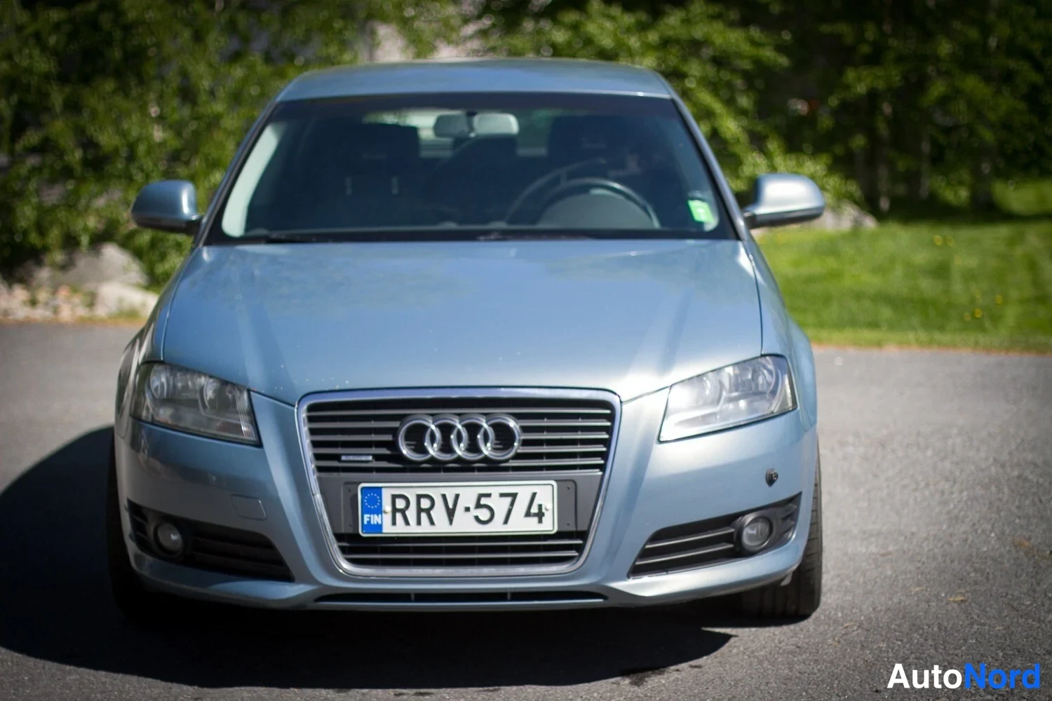 Edestä: Front view of a light blue car. The grille, headlights, and license plate are centered in the frame.