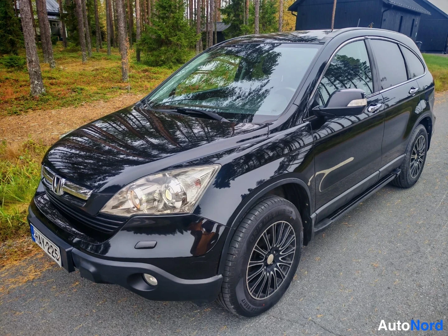 Etuviisto, nokka vasemmalle: Musta Honda CR-V edestä vasemmalta pihatiellä, koko auto näkyvissä, kori kiiltävän musta.
