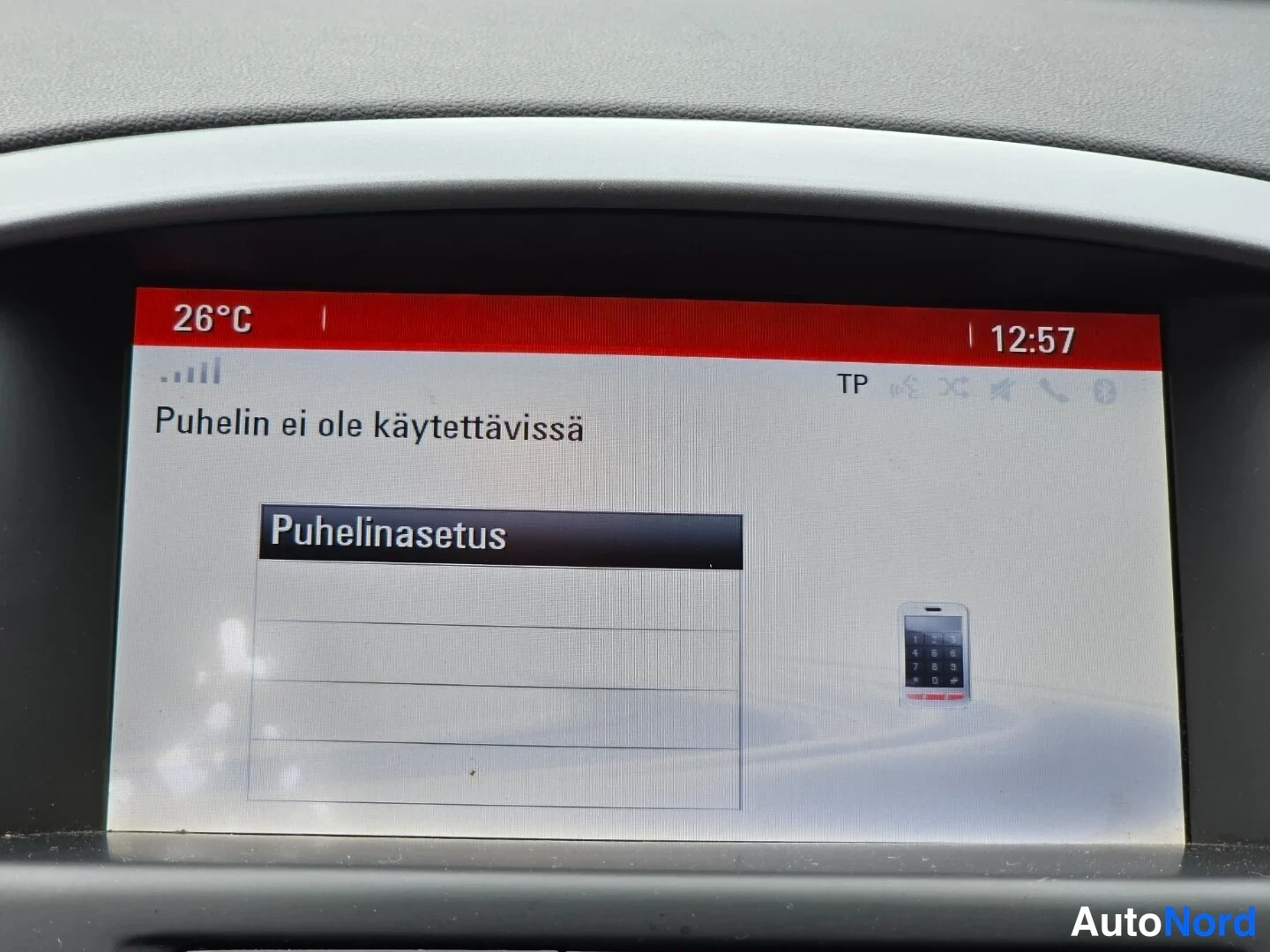 Muu: Auton kojelaudan näyttö, jossa teksti 'Puhelin ei ole käytettävissä' ja valikko 'Puhelinasetus'. Yläpalkissa lämpötila 26°C ja kello 12:57.