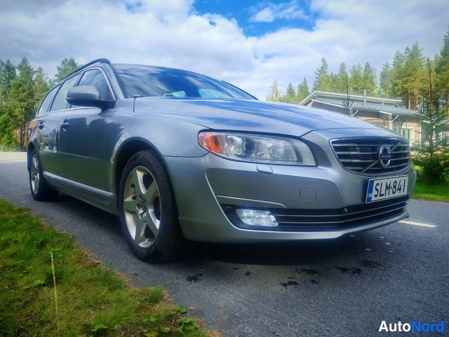Etuviisto, nokka oikealle: Etunäkökuva hieman oikealta puolelta: harmaa Volvo-asema-auto kuvattuna ruohikkoalueella taustalla. Näkyvillä ovat etuvalot, kalusto, takavalot eivät ole