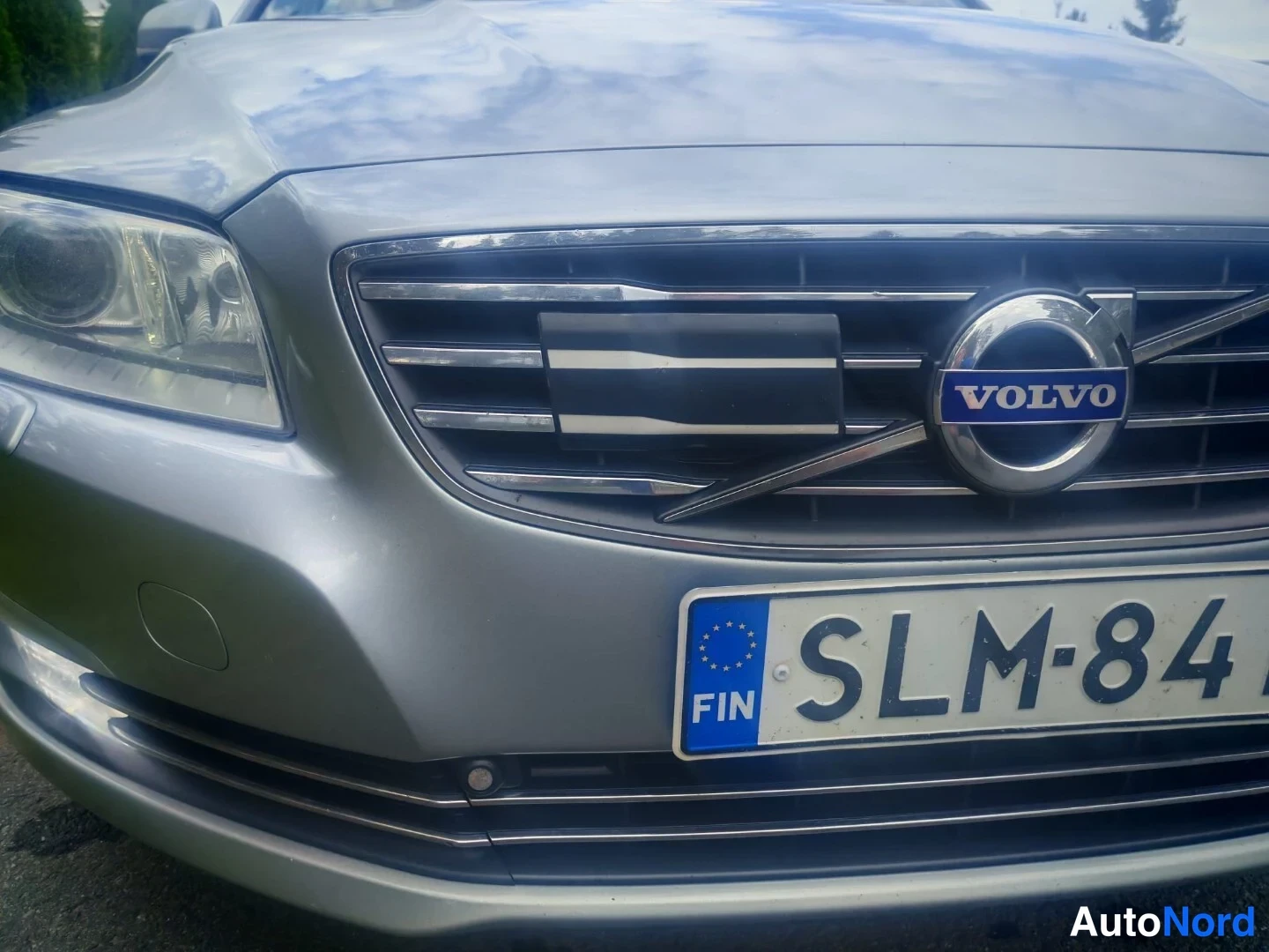 Edestä: Close-up of a silver Volvo car front showing the grille with the Volvo logo and a Finnish license plate reading