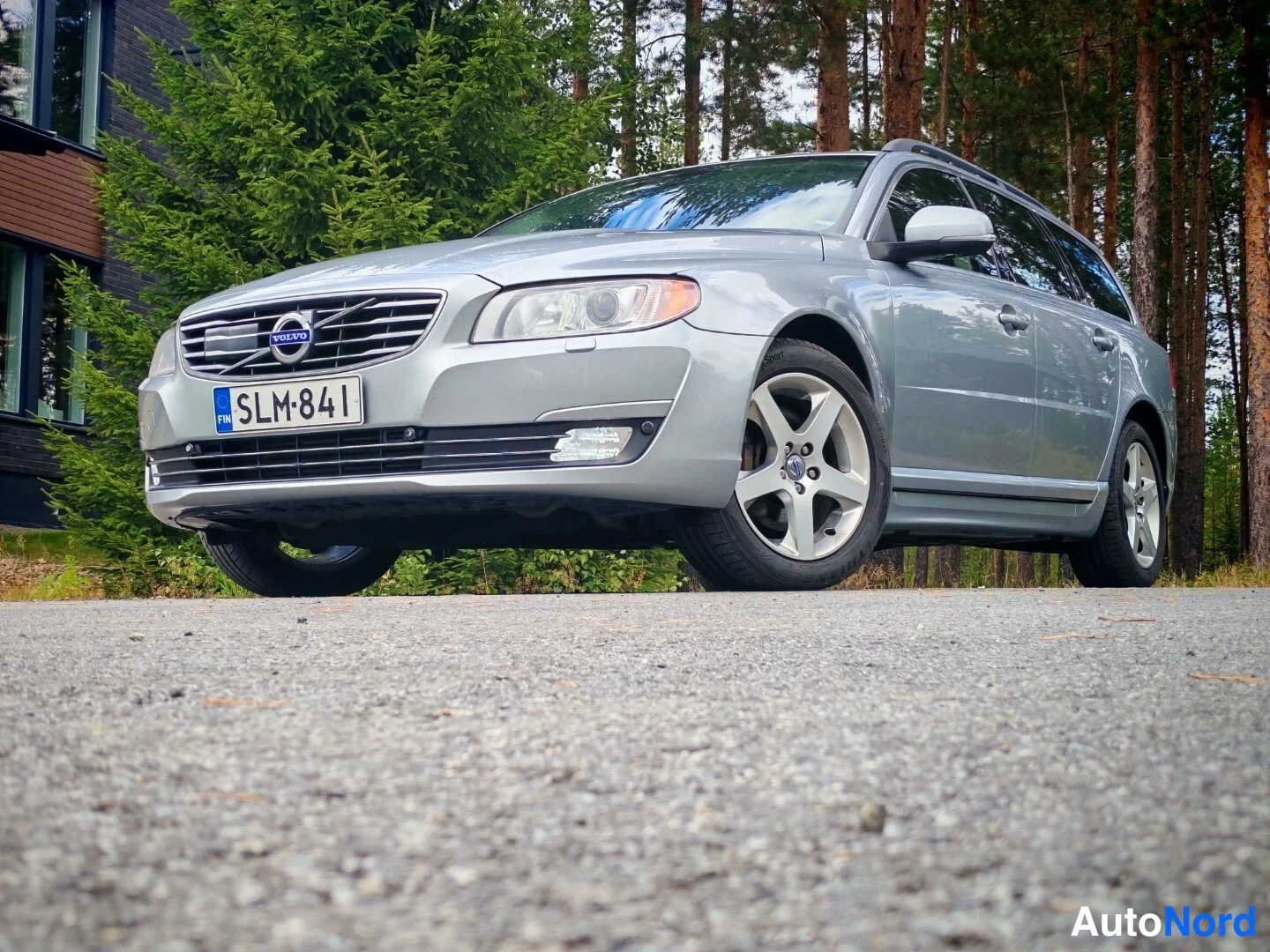 Etuviisto, nokka vasemmalle: Hopeanharmaa Volvo-farmariauto edestä kolmeneljäsosakuvassa keula vasemmalla, rekisterikilpi; kattokaiteet ja hopeavanteet näkyvät.