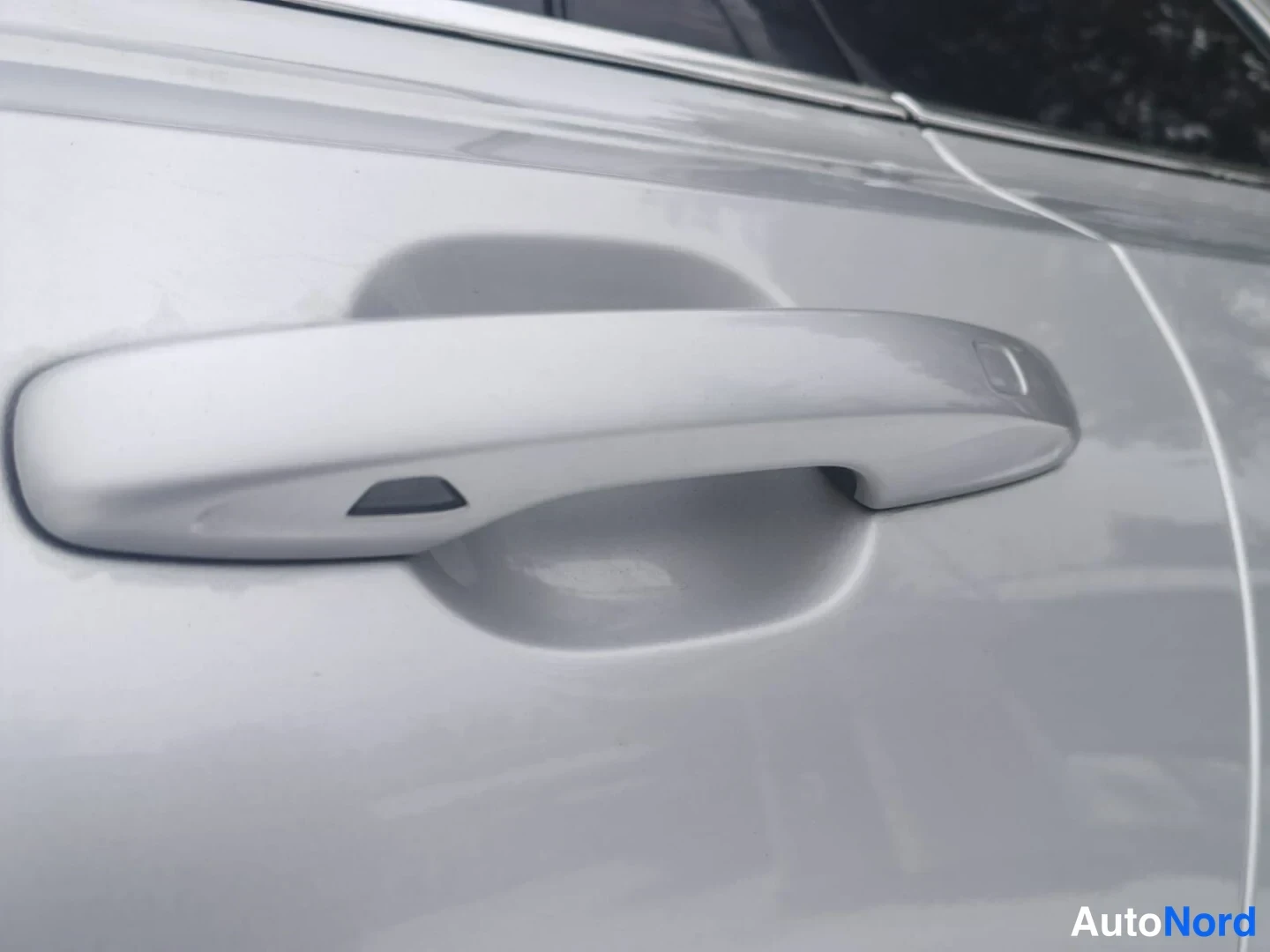 Yksityiskohta: Close-up of silver door handle with integrated keyless entry button visible on vehicle exterior panel