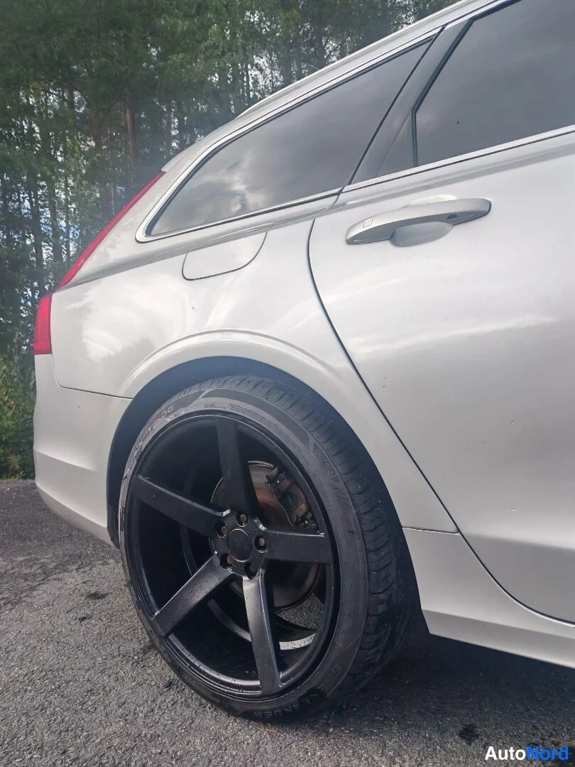 Sivulta: Auton takapyörä ja takapään kylki lähikuvassa, musta viisisakarainen vanteen alusta ja harmaa koripaneeli näkyvät.