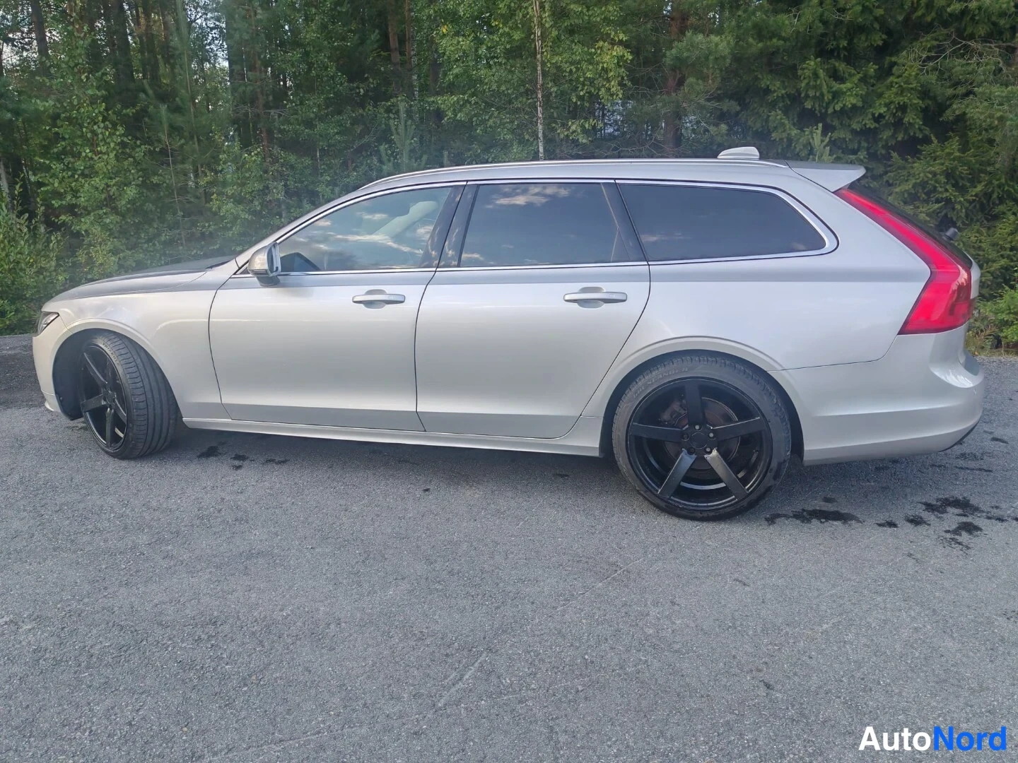 Sivulta: Silver Volvo estate shown in side profile view displaying both front and rear wheels, door handles, and side windows against forest backdrop