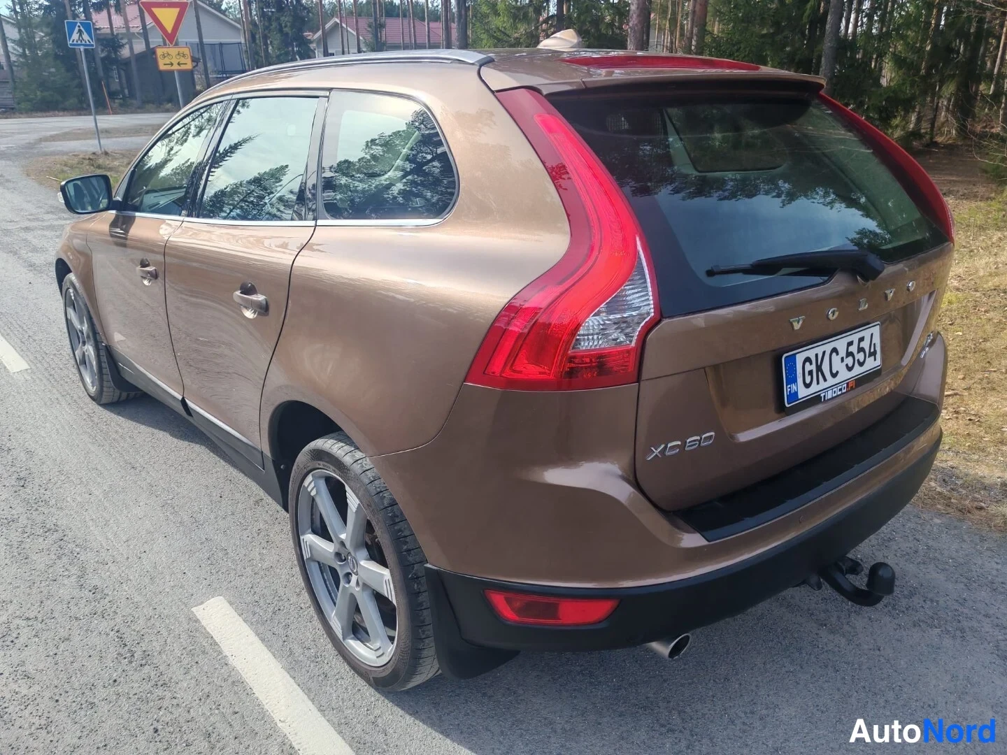 Takaviisto: Ruskean Volvo XC60:n takakulma tiellä, rekisterikilpi ja vetokoukku näkyvissä.