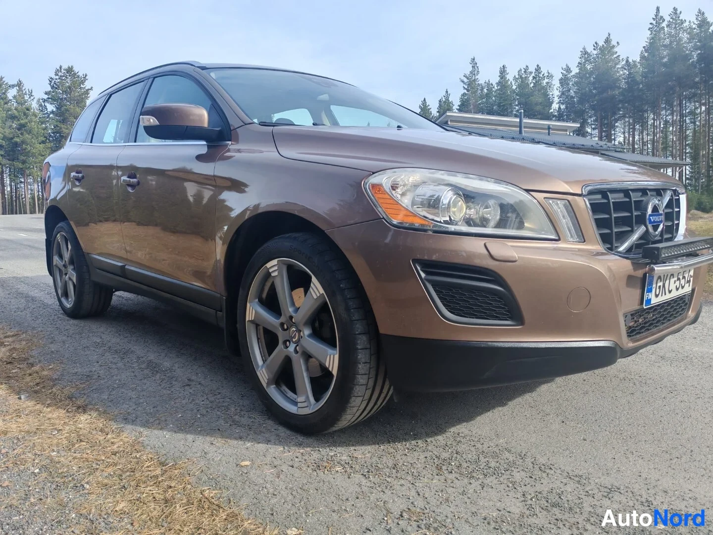 Etuviisto, nokka oikealle: Volvo XC60 edestä oikealta kuvattuna, rekisterikilpi, ruskea koriväri.