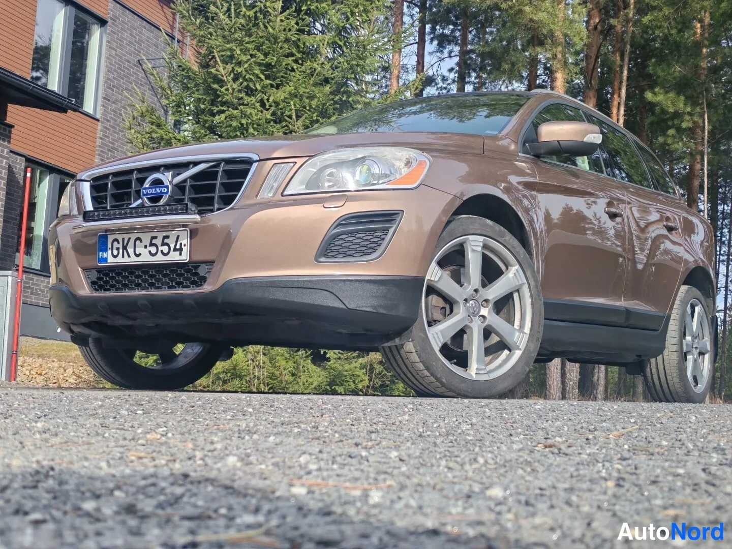 Etuviisto, nokka vasemmalle: Ruskea Volvo matalasta kuvakulmasta edestä vasemmalta, rekisterikilpi, LED-palkki puskurissa, kevytmetallivanteet.