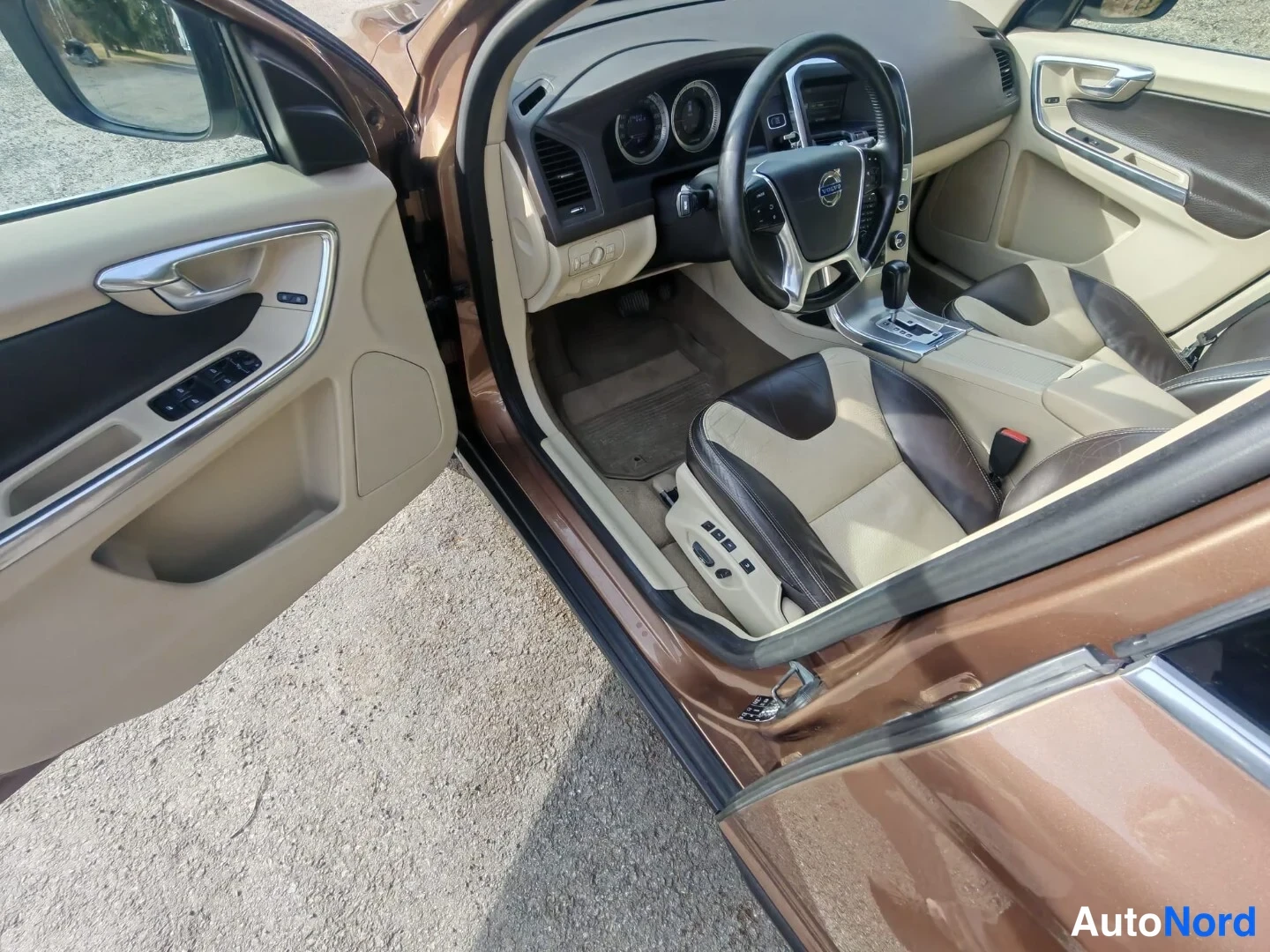 Muu: Autoon avatun kuljettajanoven takaa näkyvä ohjaamo: ruskea ja beige nahkapenkit, Volvo-ohjauspyörä ja käsintehdaskojeisto ei luettavissa; auton kori on ruskeaa.
