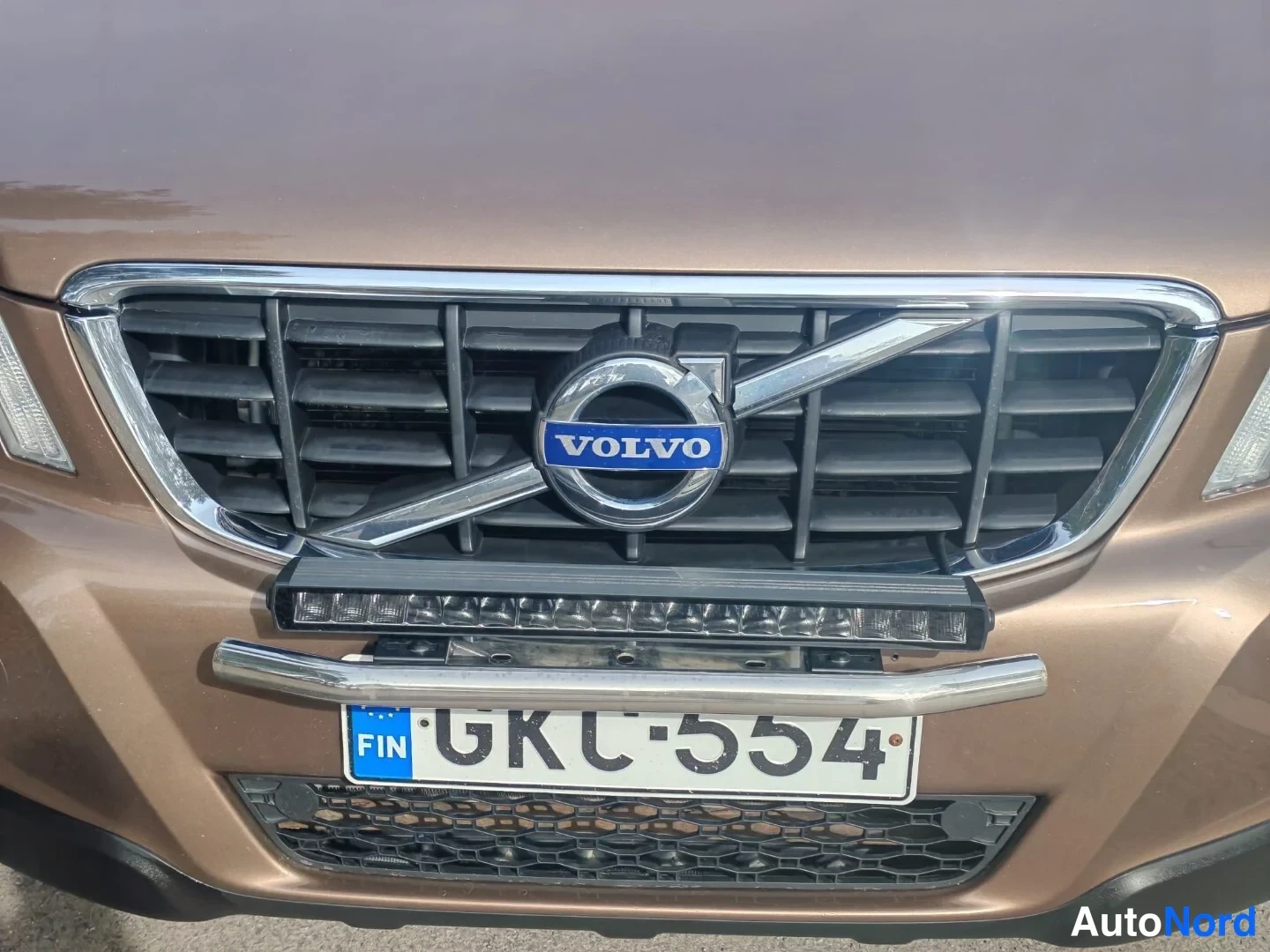 Edestä: Volvo XC60:n etusäleikkö lähikuvassa: kromikehys, VOLVO-tunnus ja etupuskurissa lisävalo ja kromikorre, rekisterikilpi.