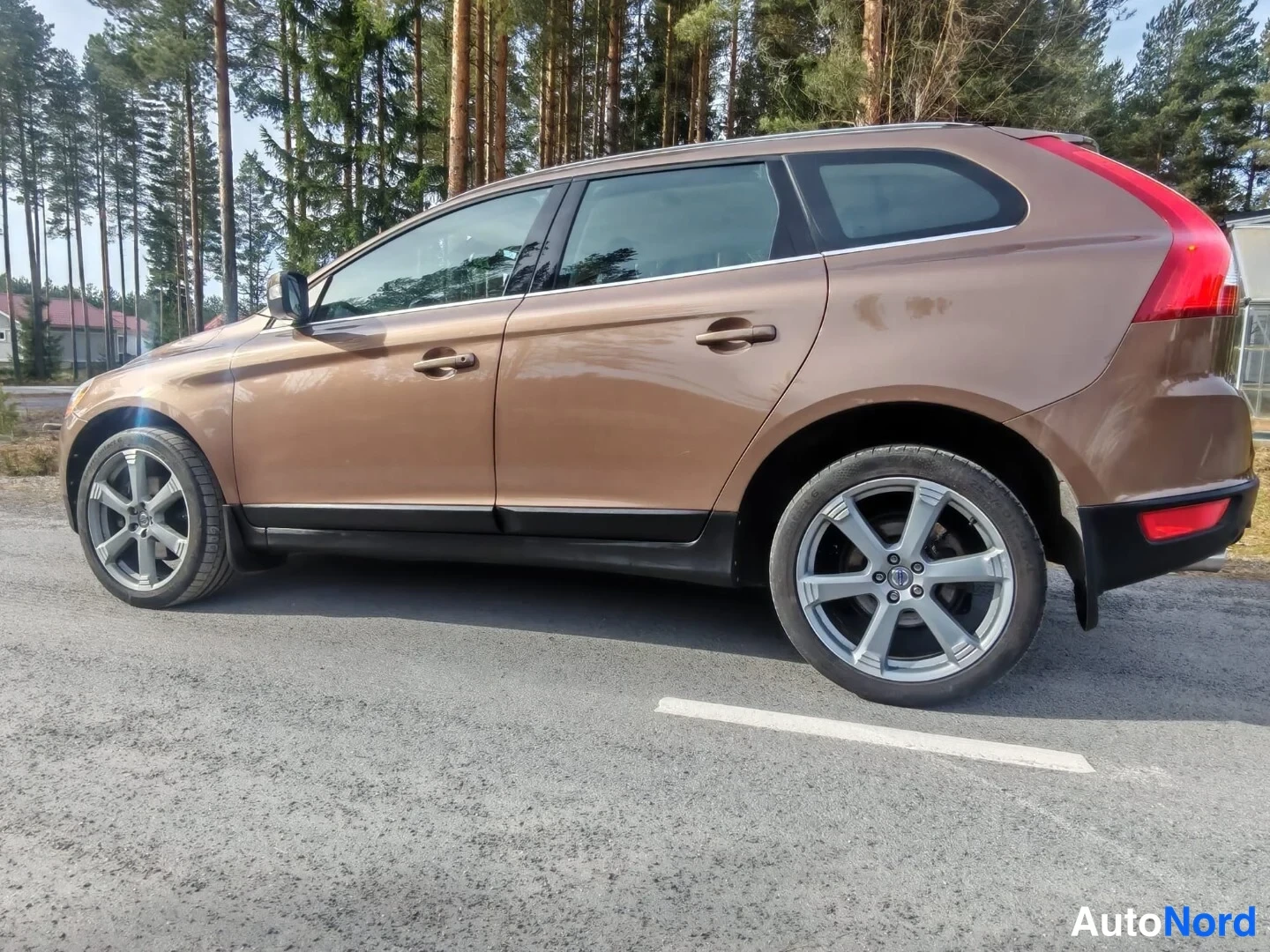 Takaviisto: Ruskea Volvo XC60 sivulta takaa päin, koko kylki ja takavalo näkyvissä, hopeiset vanteet ja katolla kromiset kaiteet.